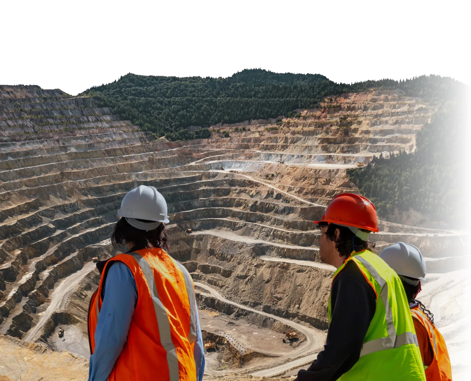 Three engineers in high-visibility vests looking out over a terraced open-pit mine